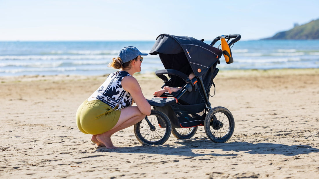 Female parent checking in on their child in a compact travel buggy on a beach during a family day out