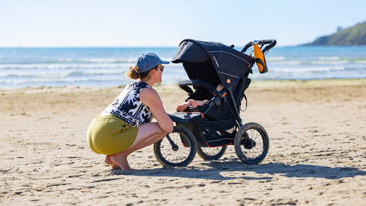 Female parent checking in on their child in a compact travel buggy on a beach during a family day out