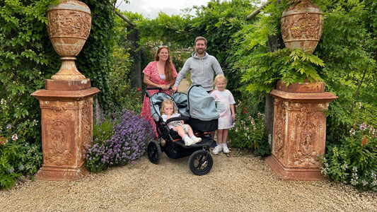 Family with a double stroller for newborn and toddler in a garden, featuring the Nipper Double V5