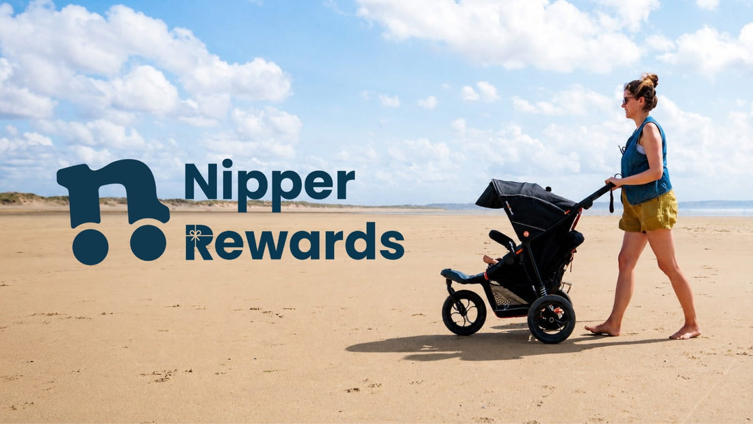 A parent pushes an Out ’n’ About Nipper buggy along a sandy beach beside the Nipper Rewards logo.