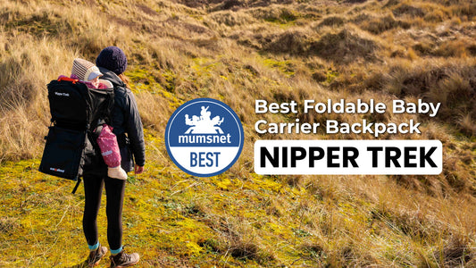 Parent carrying a child in the Nipper Trek on a grassy hillside with Mumsnet’s Best Foldable Baby Carrier Backpack badge.