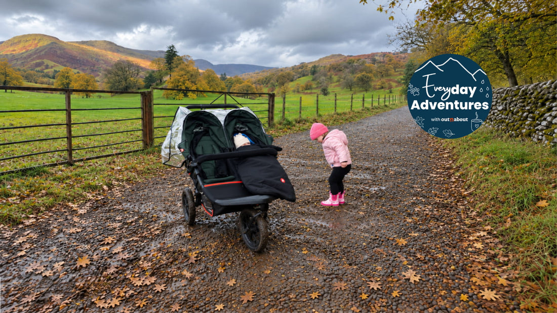 Out’n’About Nipper Double V6 pushchair on a country lane in an autumn landscape with children, featuring the Everyday Adventures campaign badge