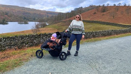 Parent with baby and toddler in their Out ’n’ About Nipper Double V6, featured in our Best Double Pram guide, on a scenic all-terrain gravel path 