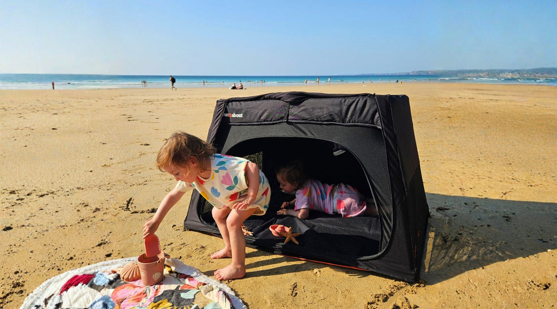 Toddlers playing on a beach beside an Out’n’About Nipper Nest travel cot