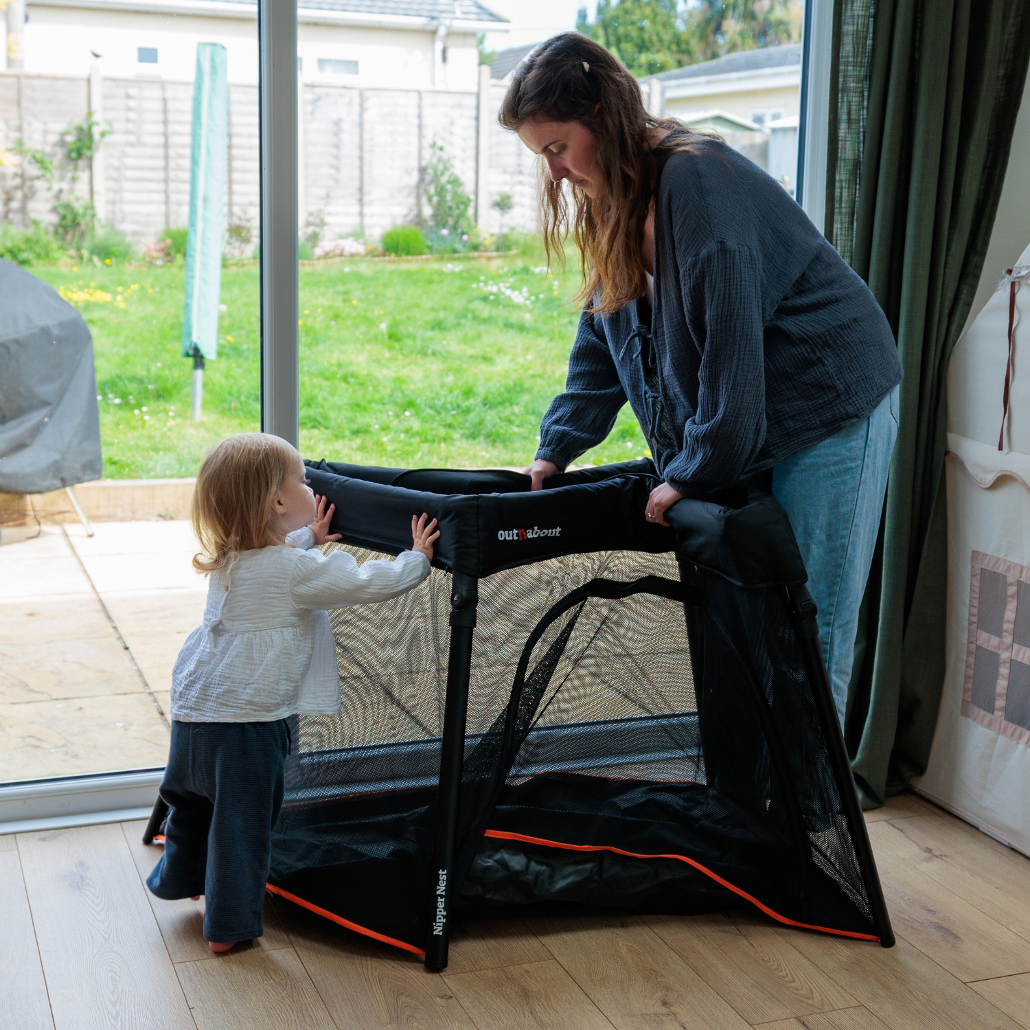 Woman and child setting up a Nipper Nest in a room with large windows.